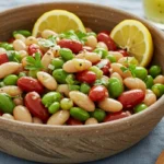 Colorful dense bean salad with mixed beans, fresh vegetables, and a zesty dressing in a large serving bowl.