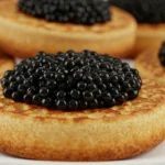 Crumpets with caviar, crème fraîche, and chives on a white marble platter.