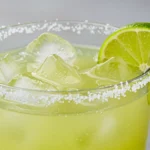 A refreshing margarita mix in a glass jar with limes, salt, and fresh mint for garnish.