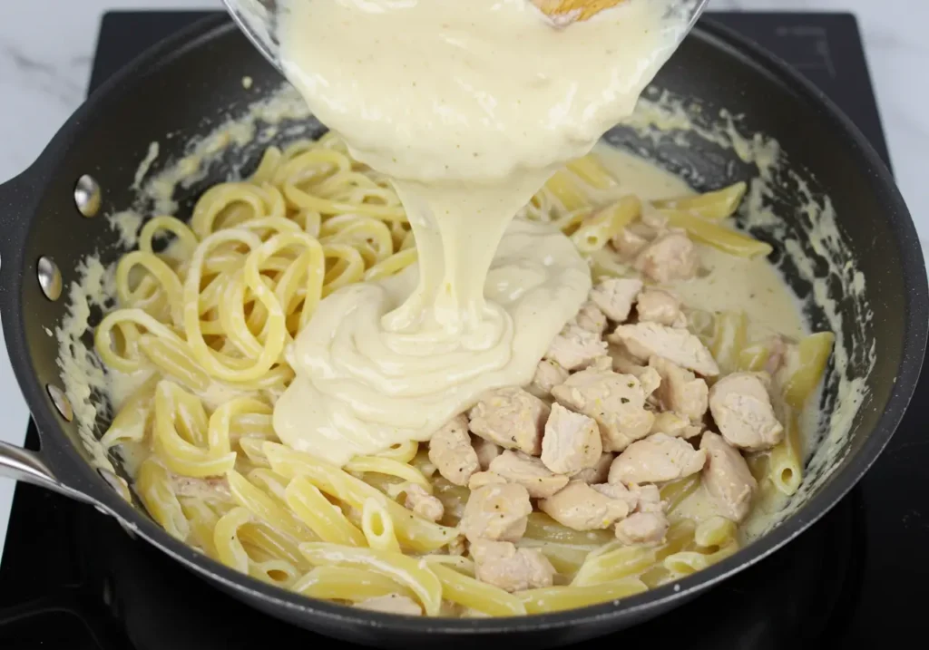 Cooked pasta added to a creamy garlic sauce with chicken, tossing everything together for a rich and flavorful finish.