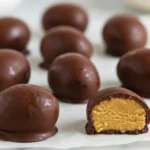 A plate of homemade peanut butter eggs with a bite taken out, revealing the creamy filling.